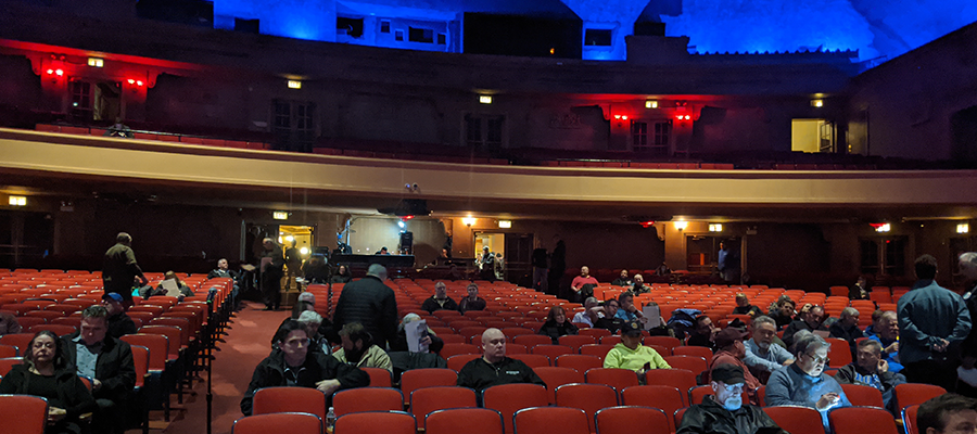 Half-full auditorium of people waiting for a public meeting to start